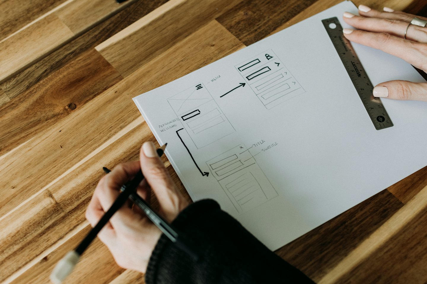 Hands sketching wireframes and user interface elements on paper.